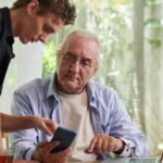A middle-aged adult helping an elderly parent while reviewing financial documents at home.