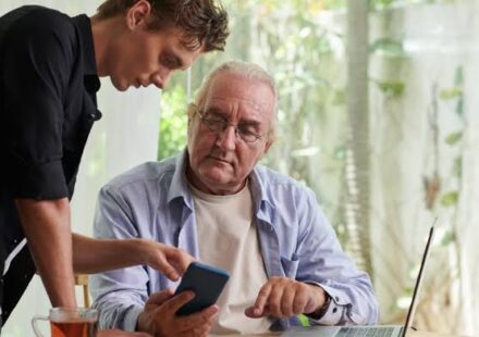 A middle-aged adult helping an elderly parent while reviewing financial documents at home.