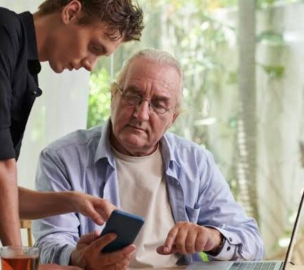 A middle-aged adult helping an elderly parent while reviewing financial documents at home.