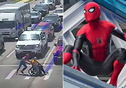 A man dressed as Spider-Man helping a wheelchair user cross a busy street