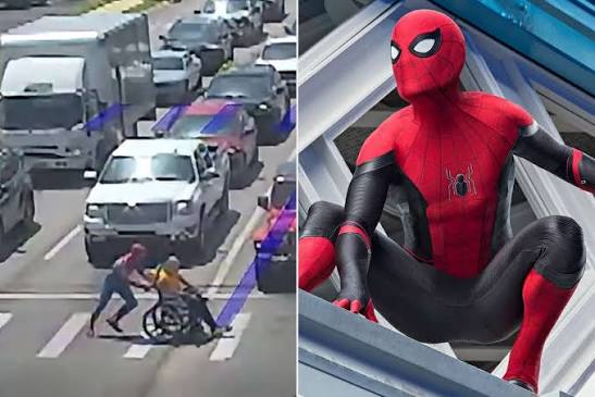 A man dressed as Spider-Man helping a wheelchair user cross a busy street