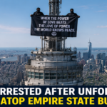 Two masked individuals standing on the Empire State Building antenna while holding a large banner before being arrested.