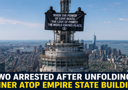 Two masked individuals standing on the Empire State Building antenna while holding a large banner before being arrested.